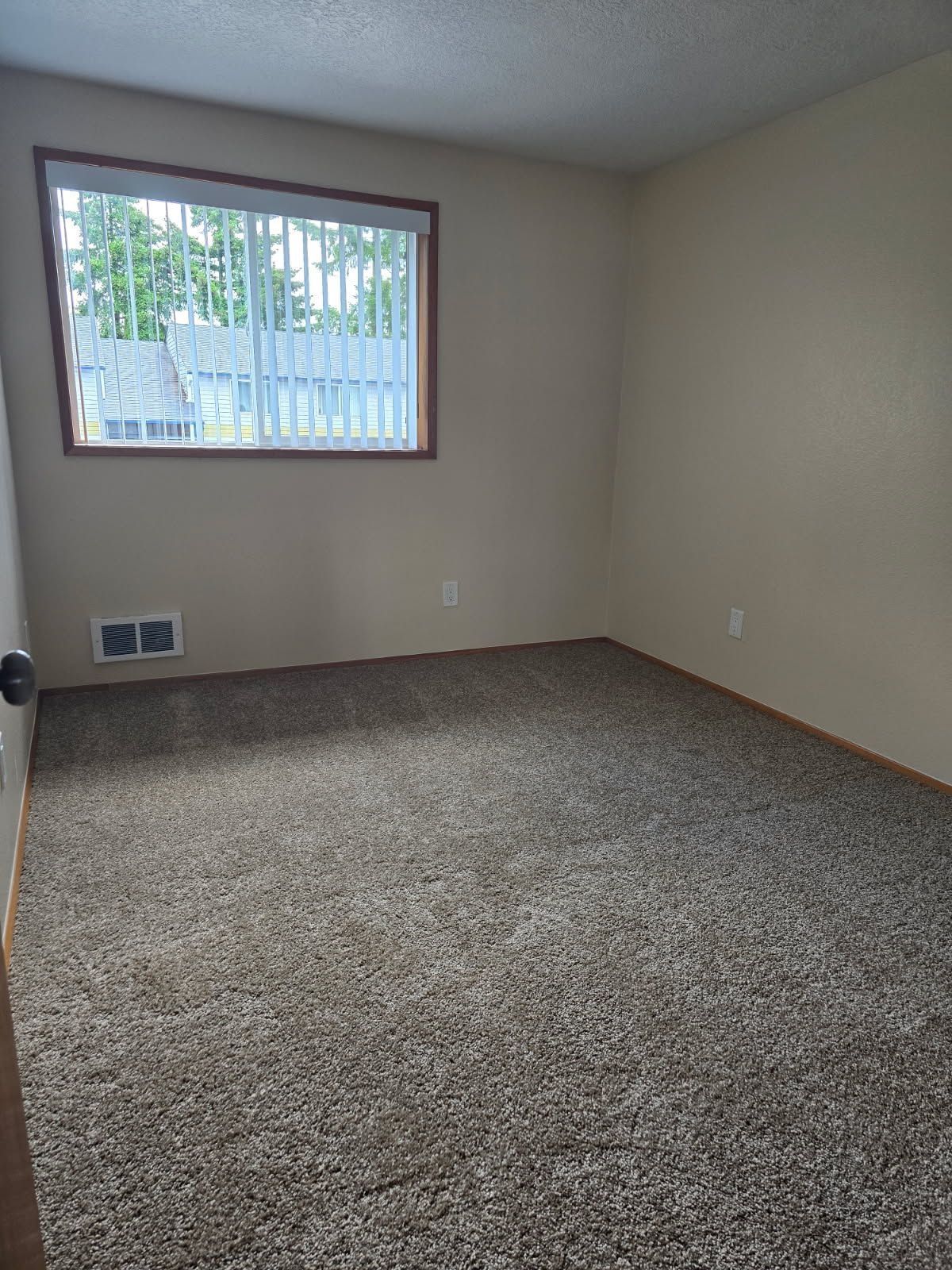 Empty beige bedroom with carpeted floor and a window showing trees outside