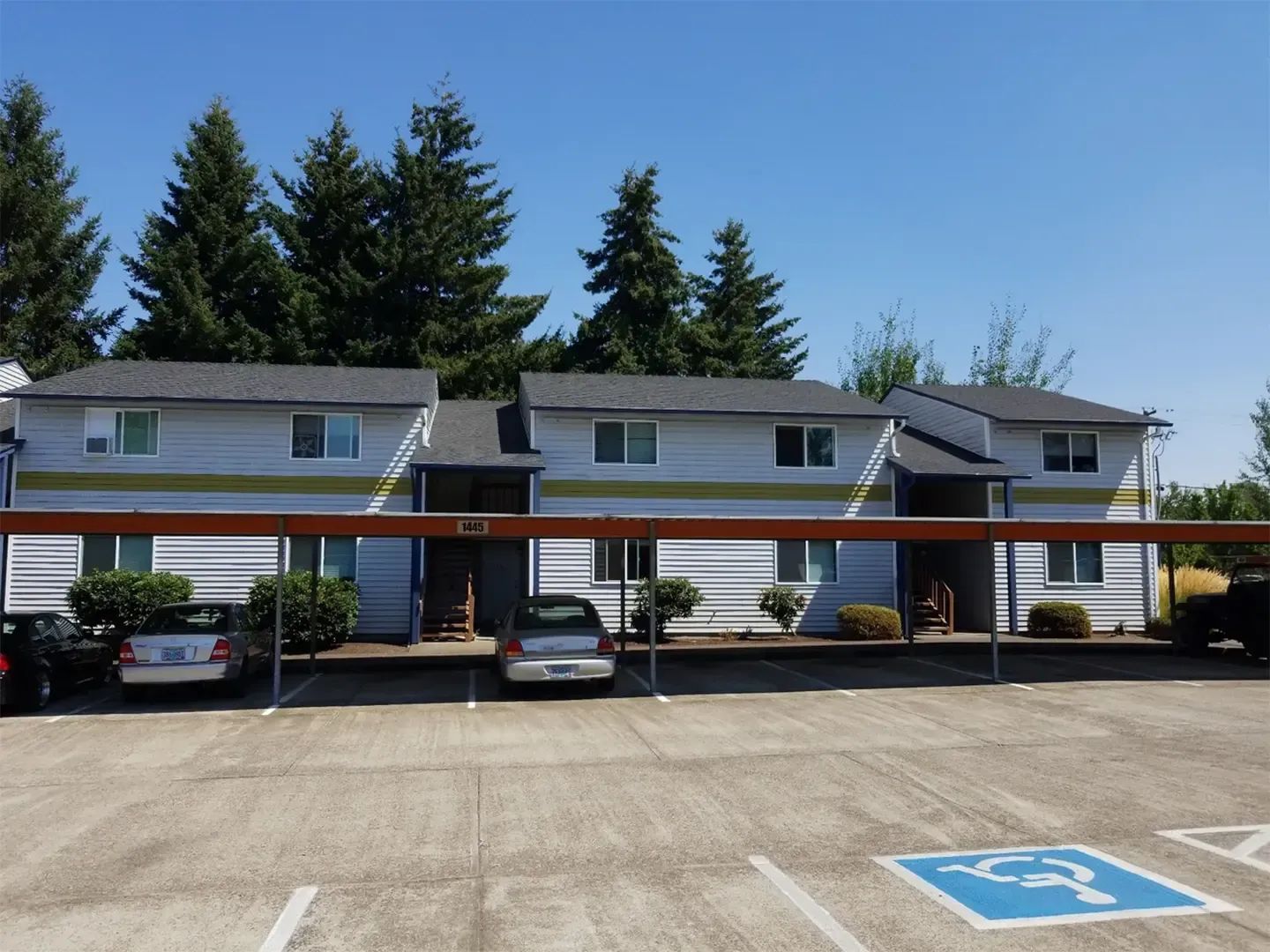 Apartment building with covered parking, cars, and a handicapped parking space in front