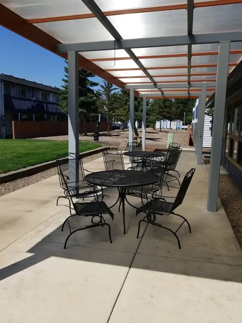 Covered outdoor patio with black metal tables and chairs on a concrete walkway beside a building.