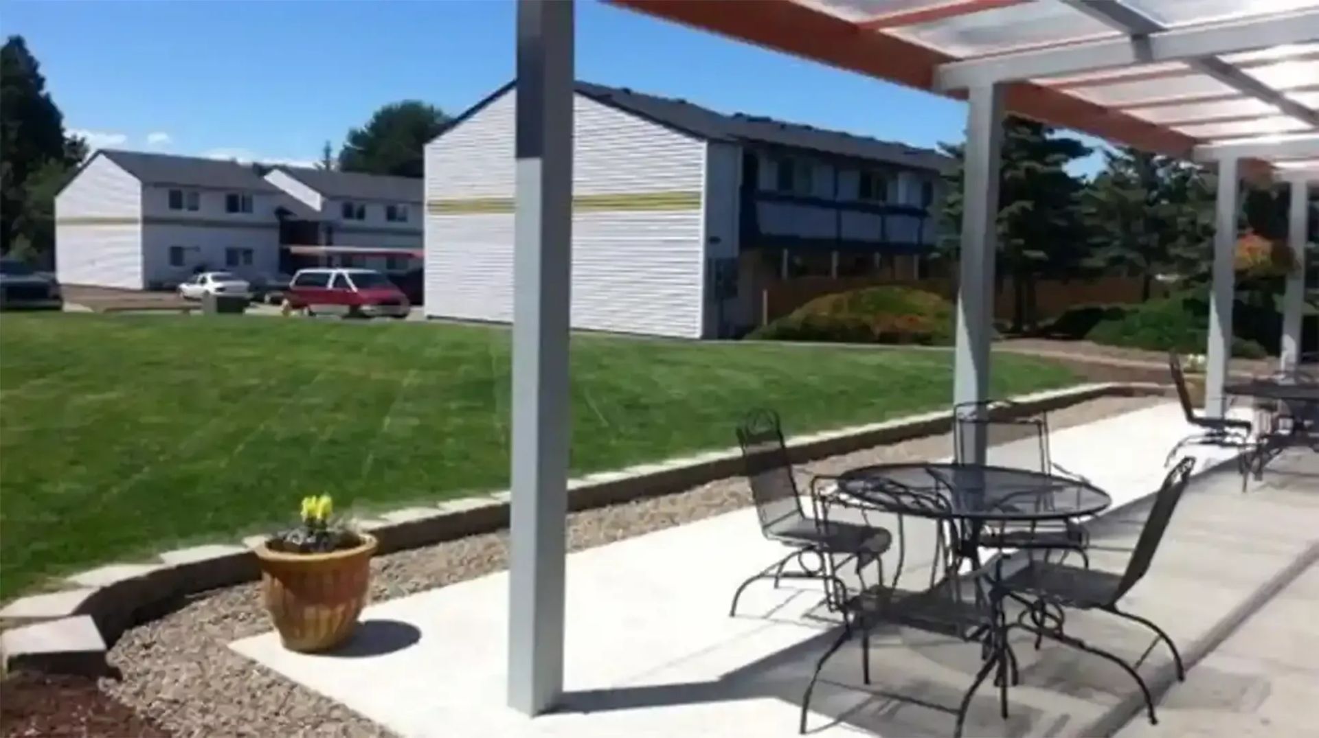 Outdoor patio with metal tables and chairs beside apartment buildings and a grassy lawn