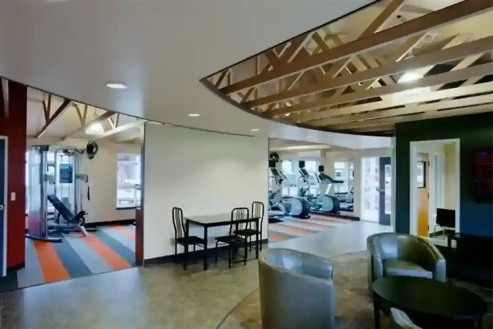 Open gym lounge with seating, wood-beam ceiling, and exercise machines visible through large openings