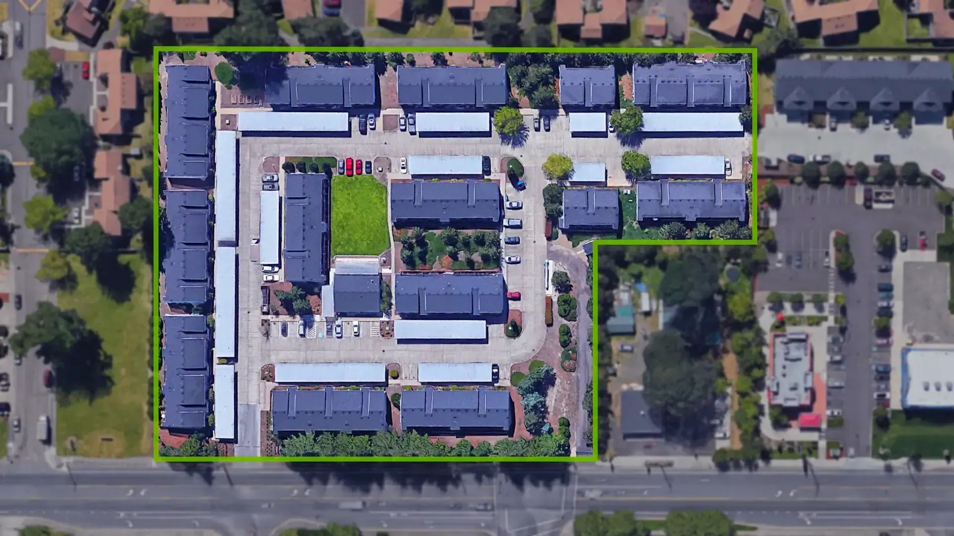 Aerial view of a complex of low buildings, parking lots, and trees along a road.