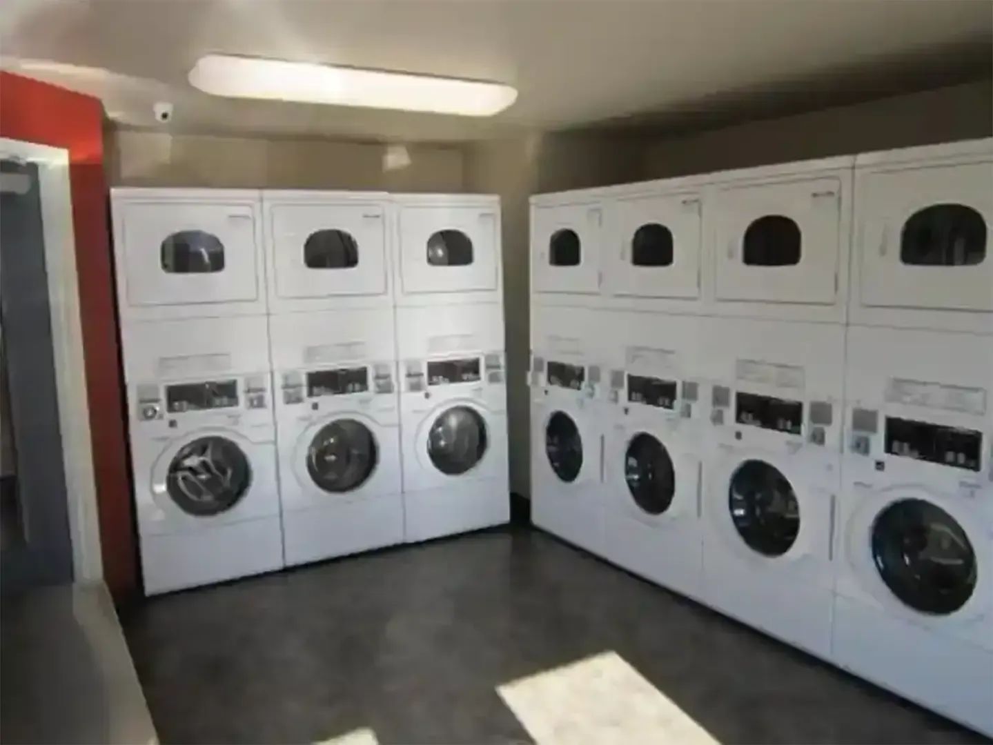Coin-operated laundry room with rows of white washers and dryers and a dark floor.
