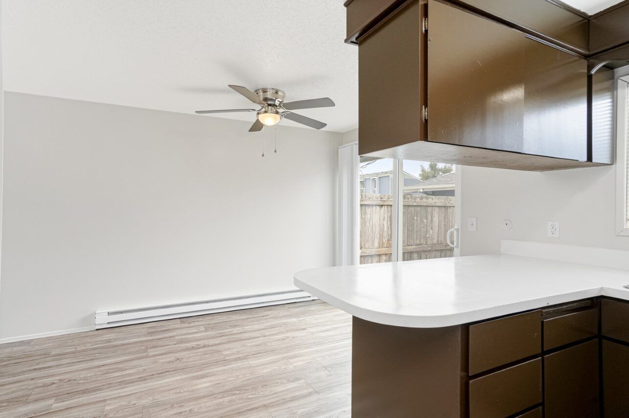 Empty modern kitchen with white counters, dark wood cabinets, and a ceiling fan in an open living space