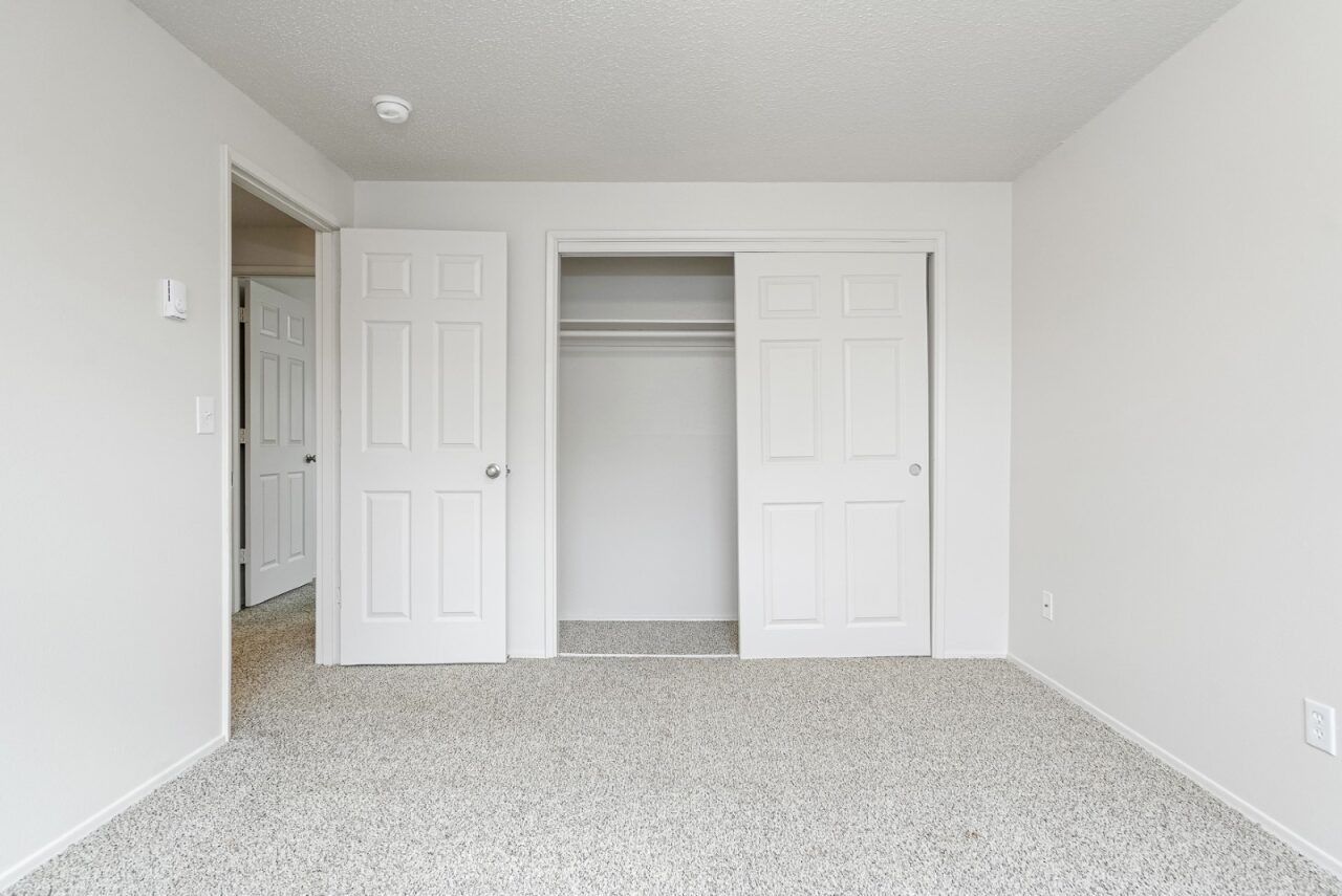 Empty white bedroom with open closet and carpeted floor