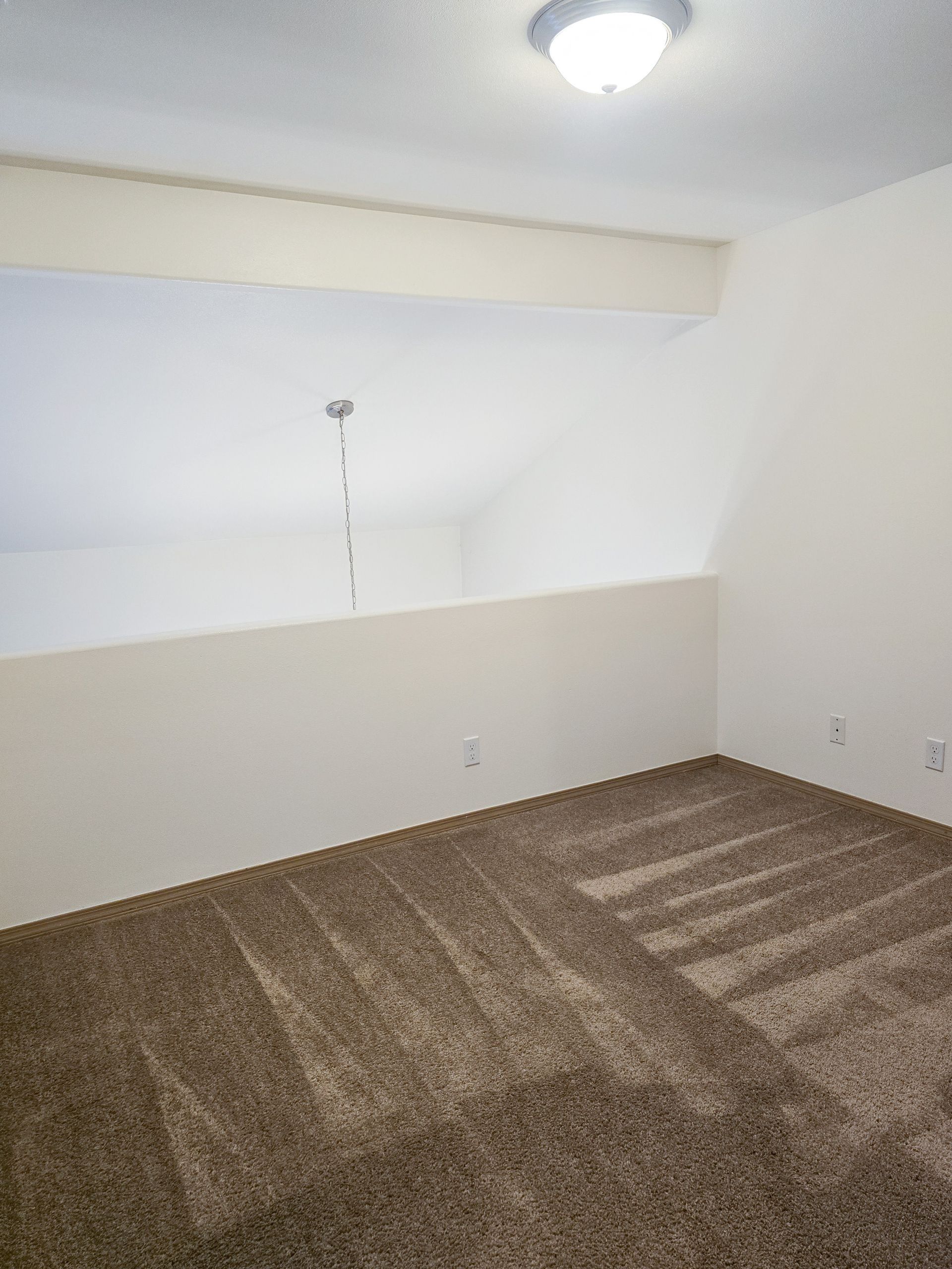 Empty carpeted room with white walls and a ceiling light, plus a small window ledge.