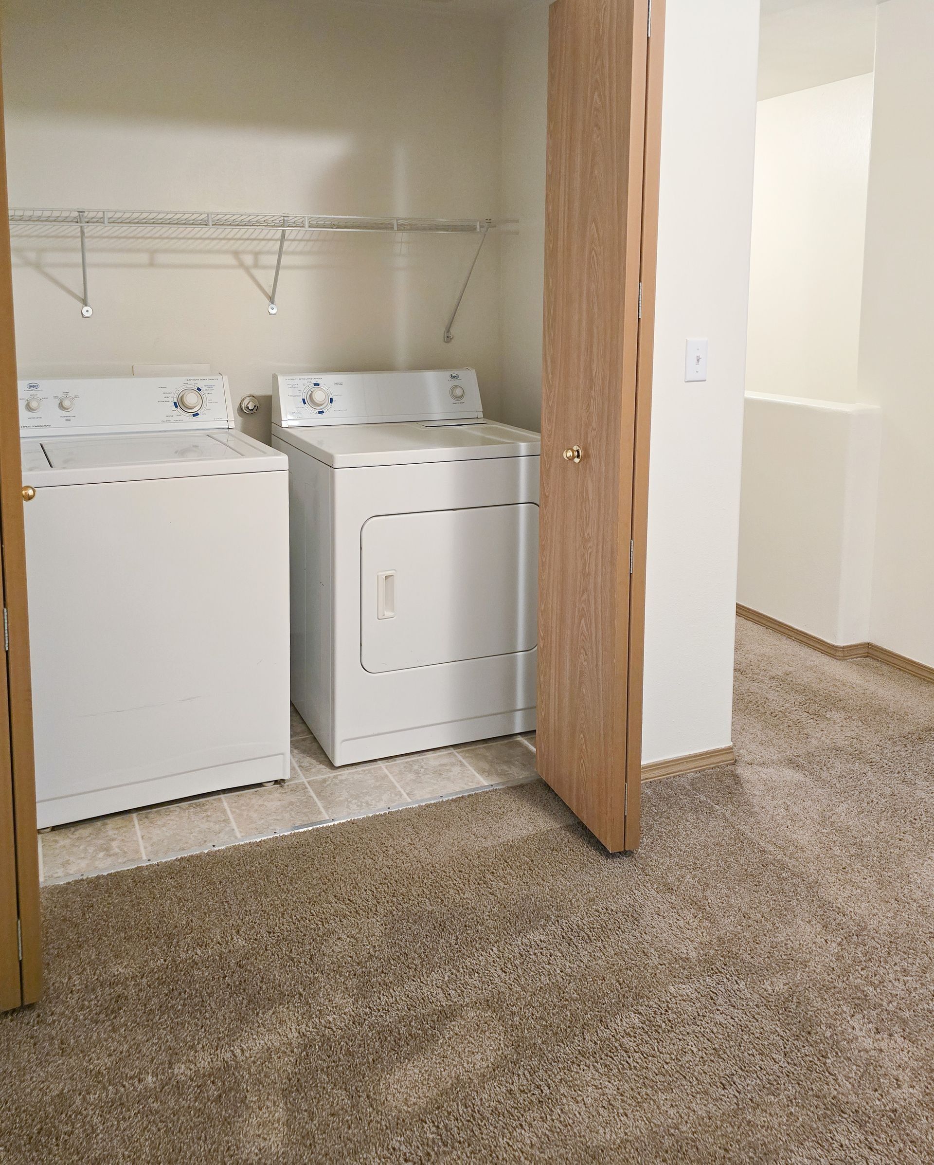 Laundry room with white washer and dryer, wire shelves, and a partially open wood door.