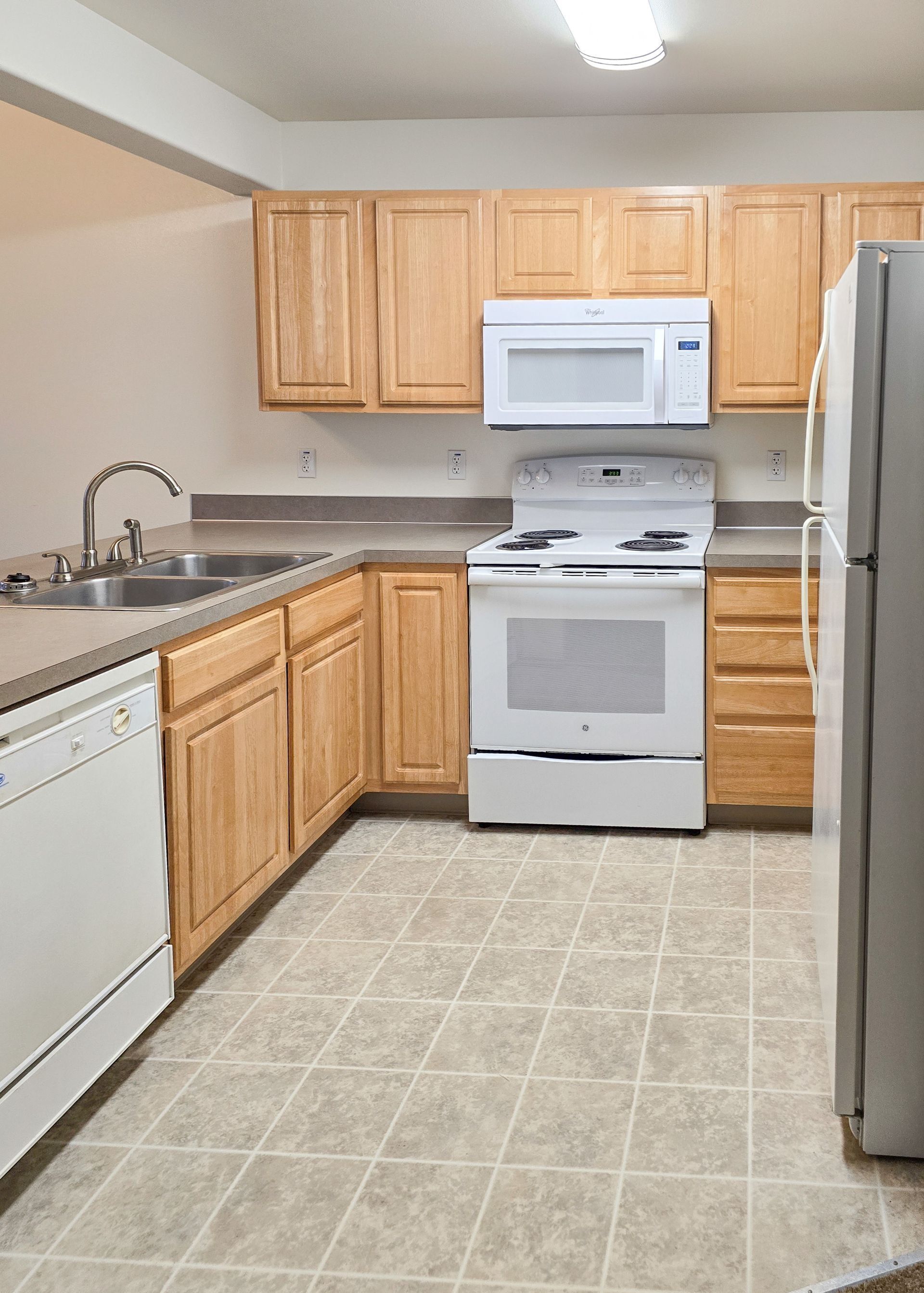 Small kitchen with wood cabinets, white appliances, and a tiled floor.