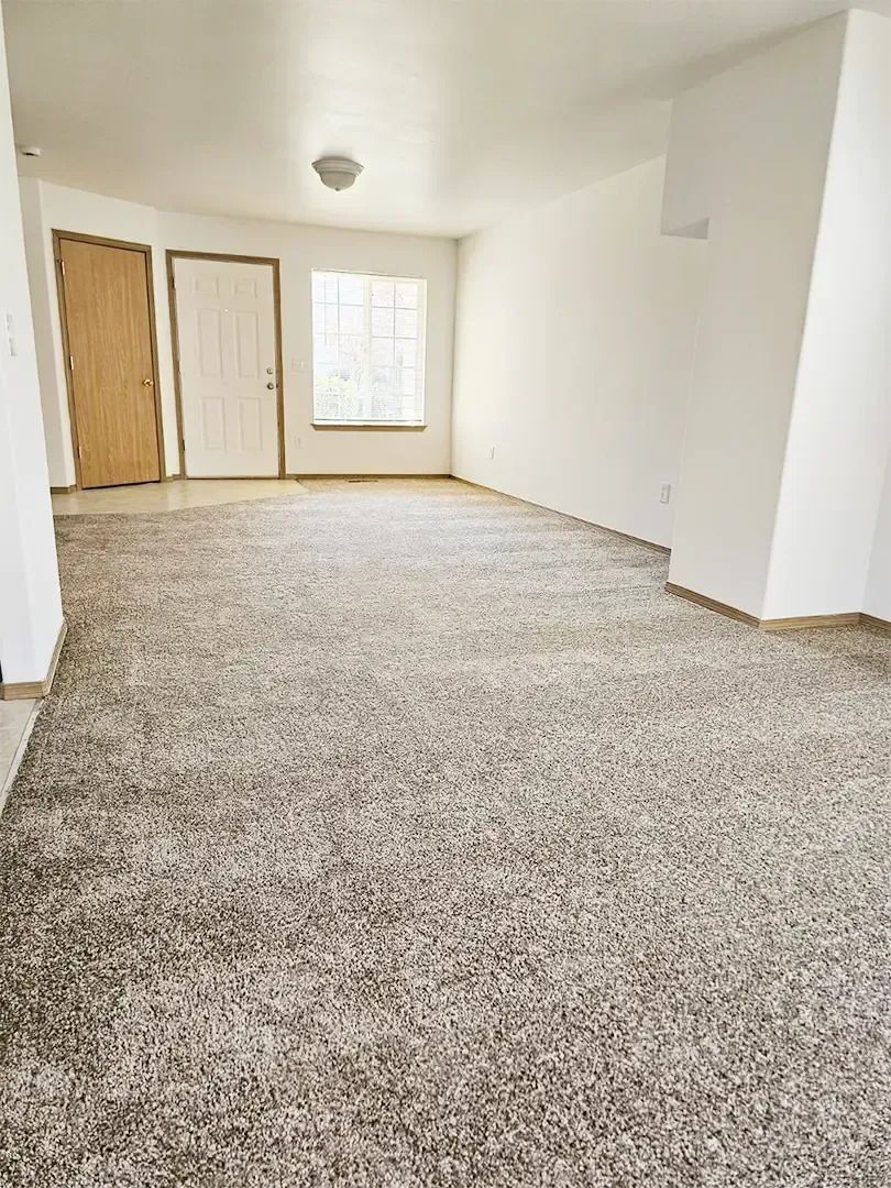 Empty carpeted room with white walls, a window, and two closet doors at the far end