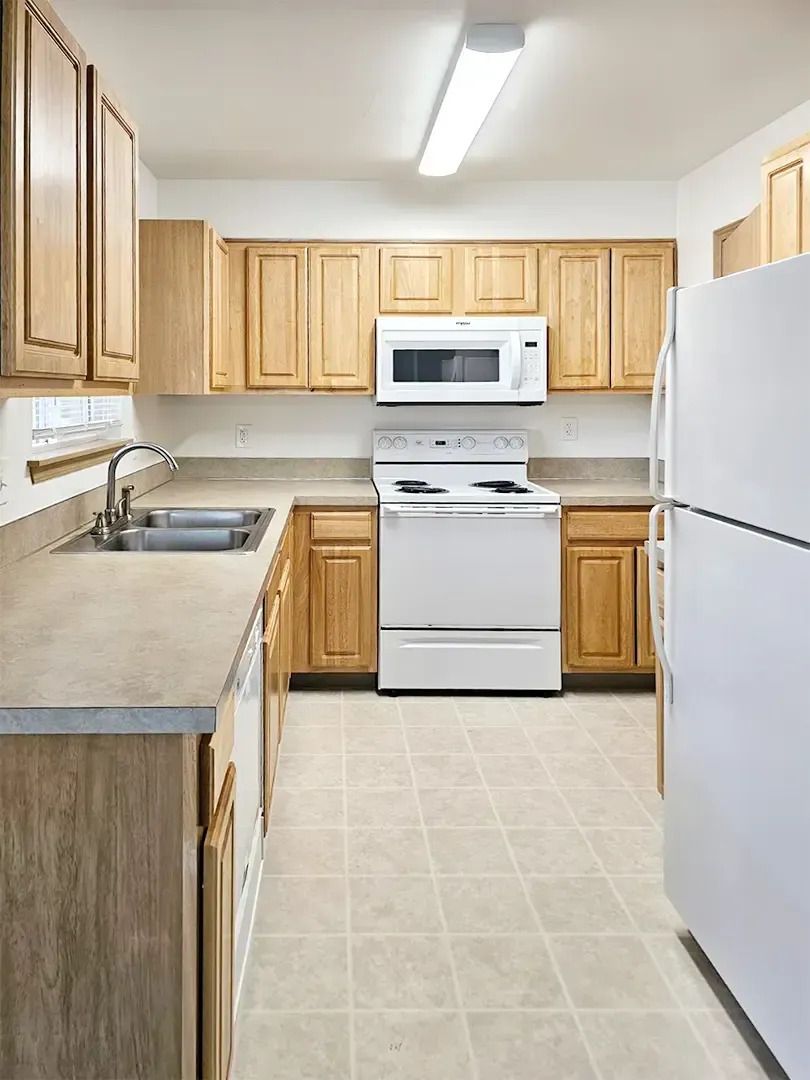 Bright kitchen with white appliances, wood cabinets, gray counters, and beige tile floor