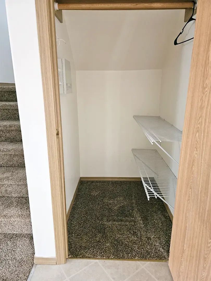 Empty walk-in closet with wire shelves, beige walls, and patterned carpet flooring.