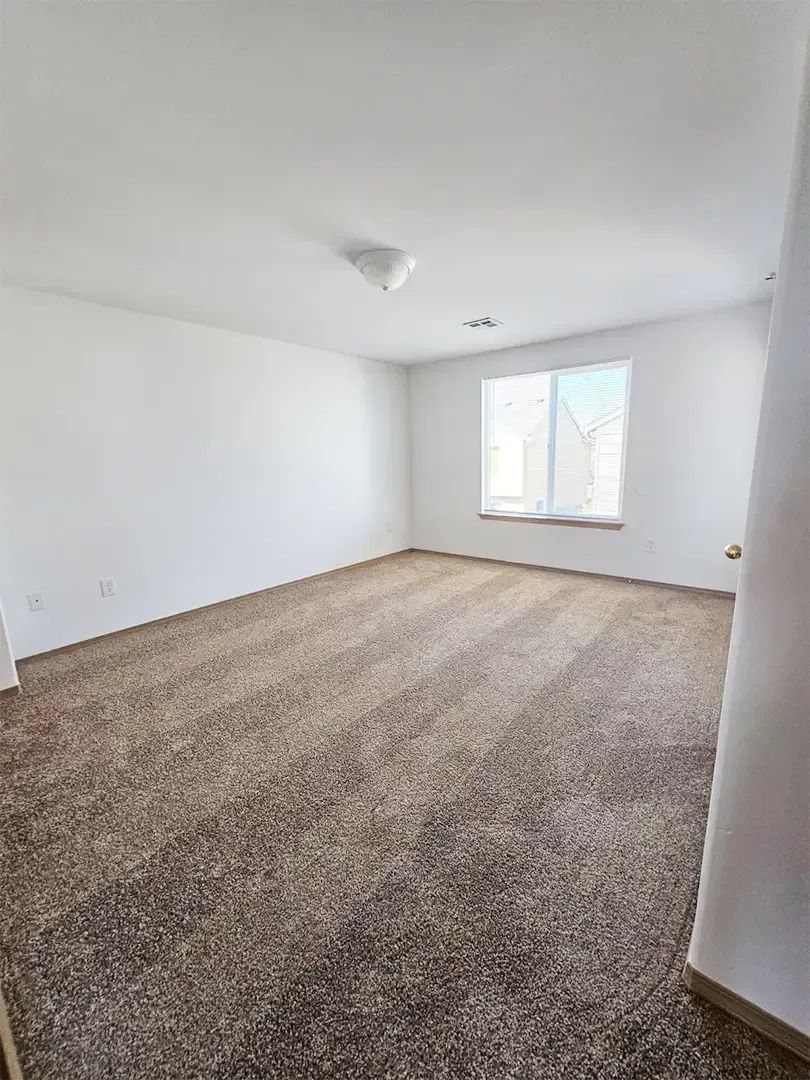 Empty carpeted room with white walls, ceiling light, and a window letting in daylight.
