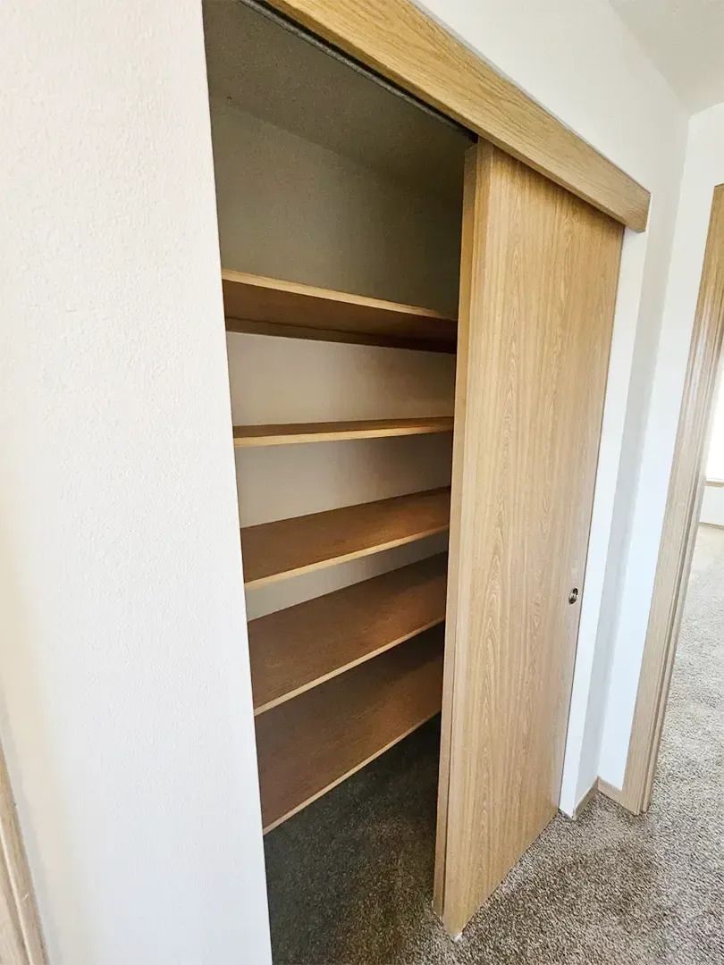 Open closet with empty wooden shelves and sliding door, viewed from a carpeted hallway