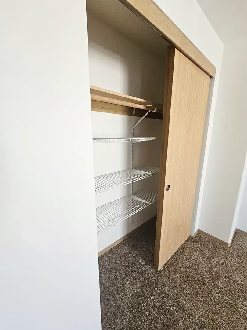 Open closet with white wire shelves and a sliding wooden door in a carpeted room