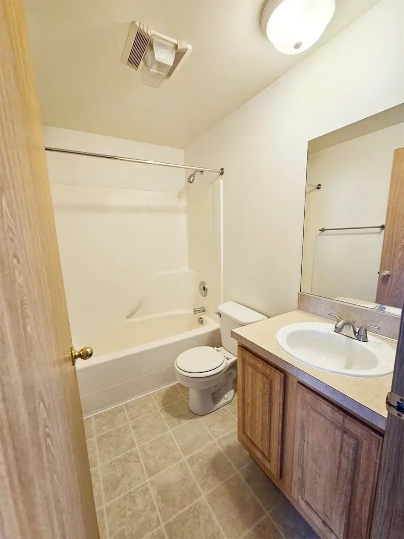 Small bathroom with a tub, toilet, sink vanity, and wall mirror.