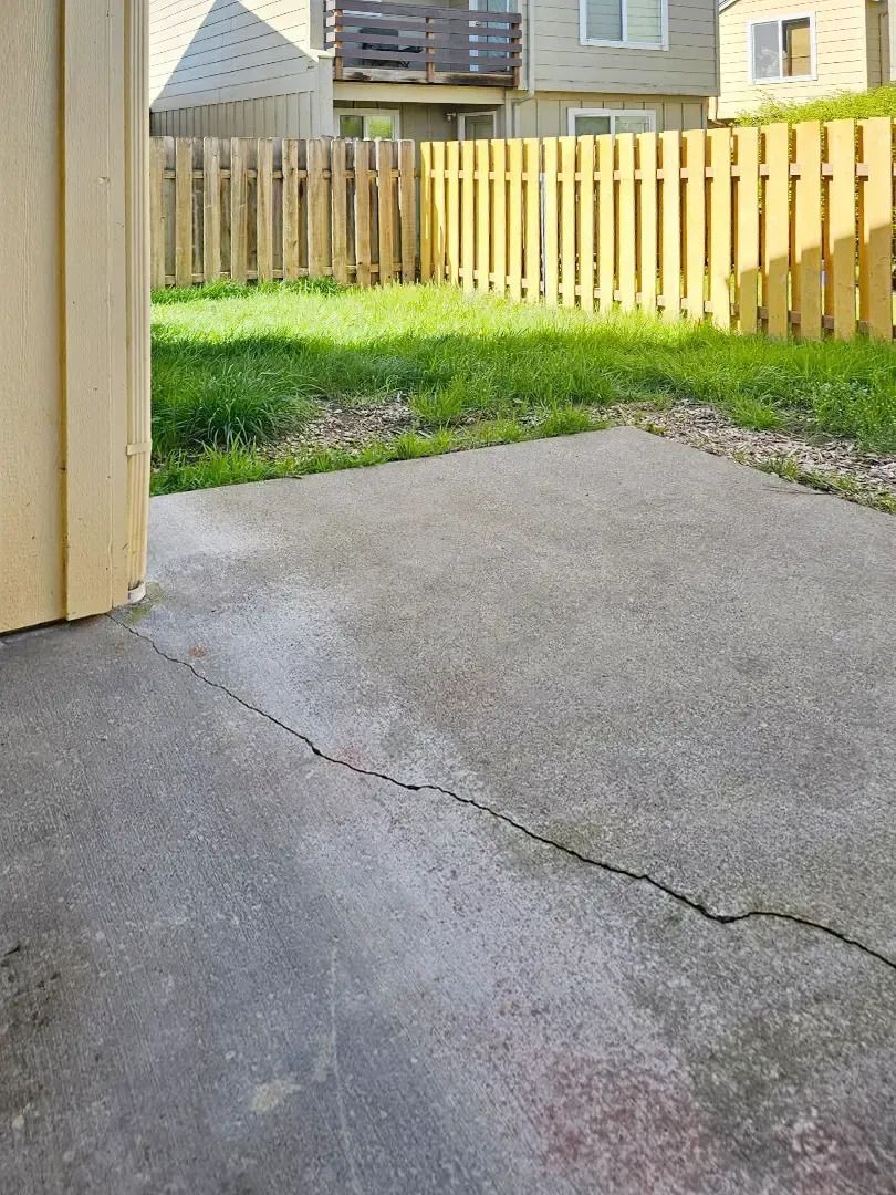 Cracked concrete patio beside a wooden fence and patchy grass in a backyard
