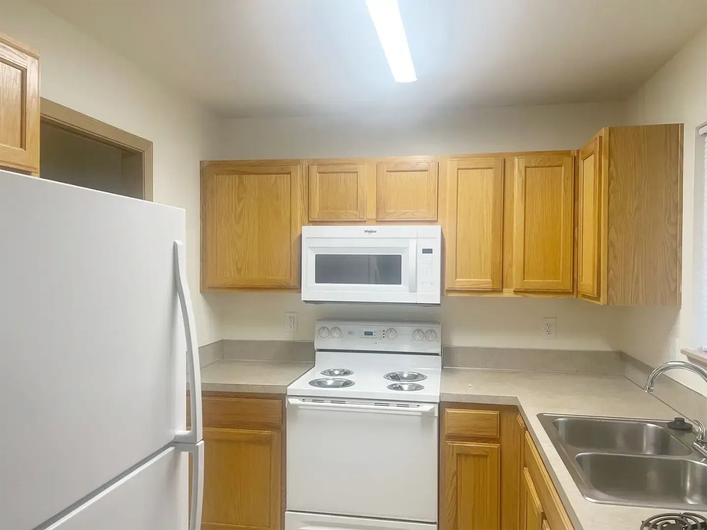 Small kitchen with white appliances, light wood cabinets, and a double sink.