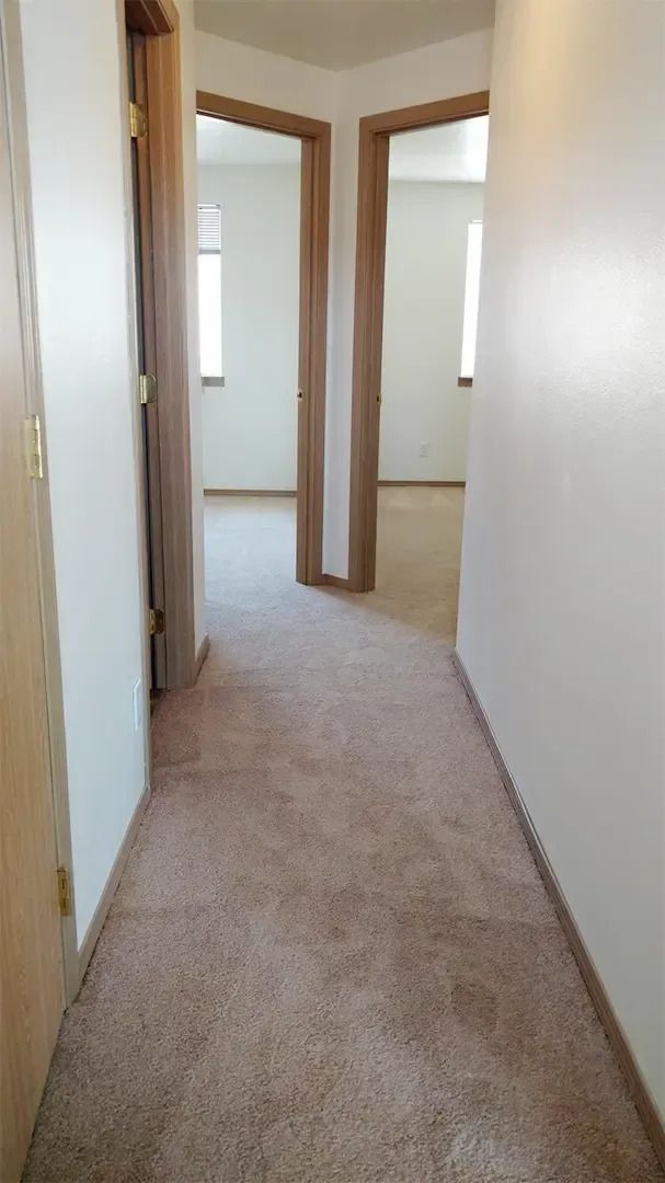 Narrow beige-carpeted hallway with wooden doorframes and doorways leading into bright rooms