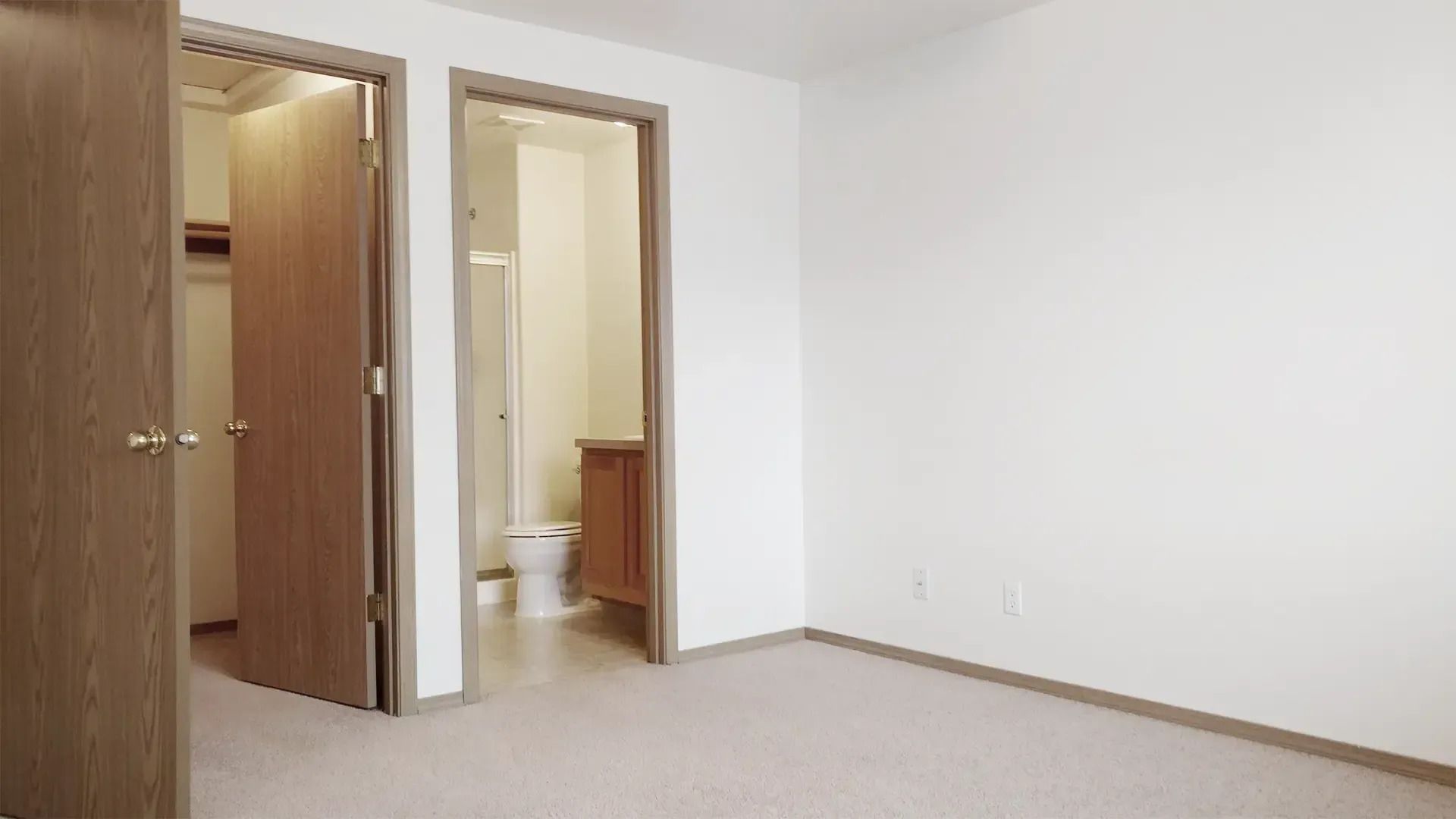 Empty beige room with two open wooden doorways and a carpeted floor.