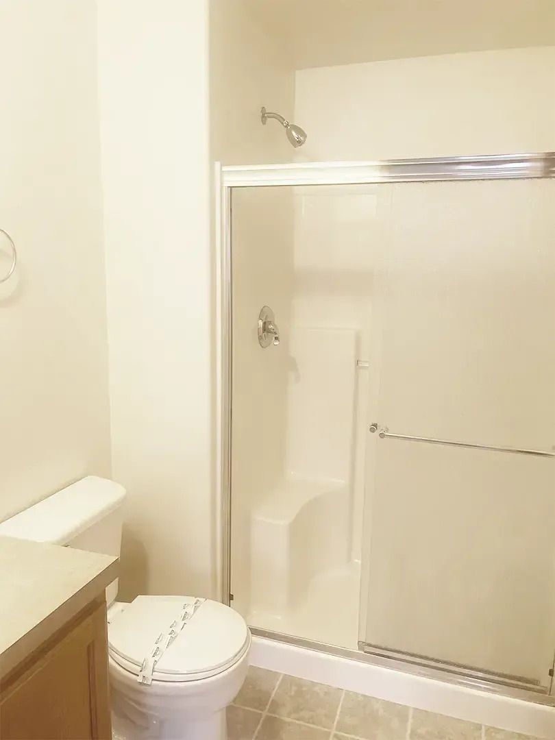 Bathroom with toilet, shower stall, and vanity in a small beige room.