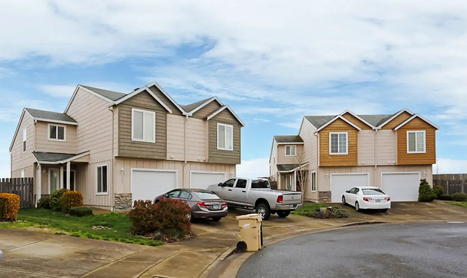 Suburban street with two tan houses, parked cars, and a cloudy sky