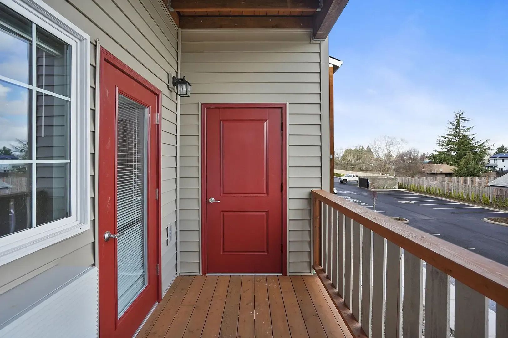 Covered porch with red doors, railing, and wooden deck overlooking a neighborhood street.