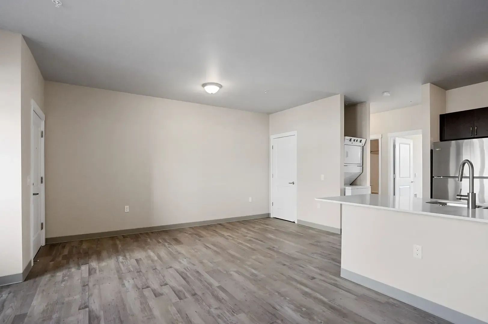 Empty modern living room and kitchen with gray wood flooring and white walls