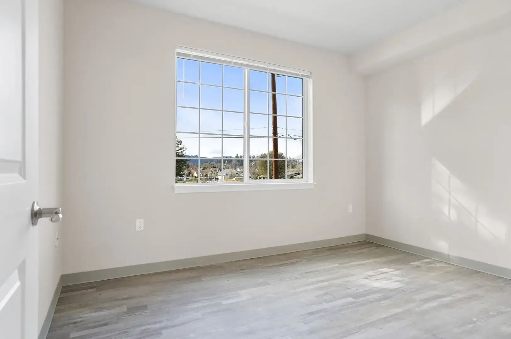 Empty white bedroom with a window and light wood flooring