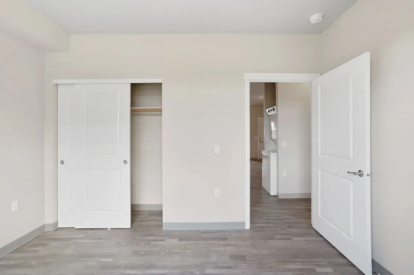 Empty white bedroom with open closet and bathroom door, gray wood floor