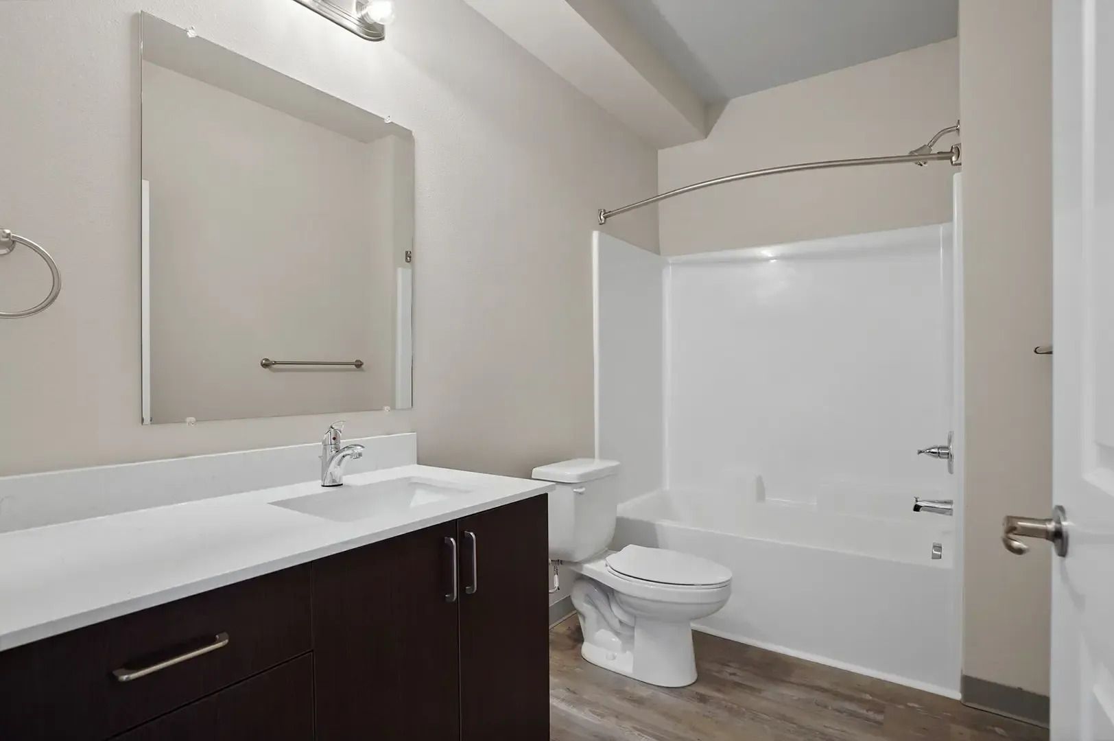 Modern white bathroom with dark vanity, mirror, toilet, and shower tub.