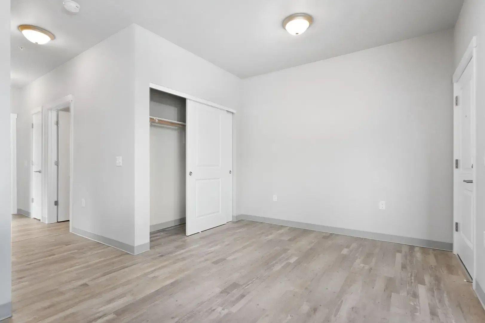 Empty white bedroom with light wood floors, open closet, and recessed ceiling lights
