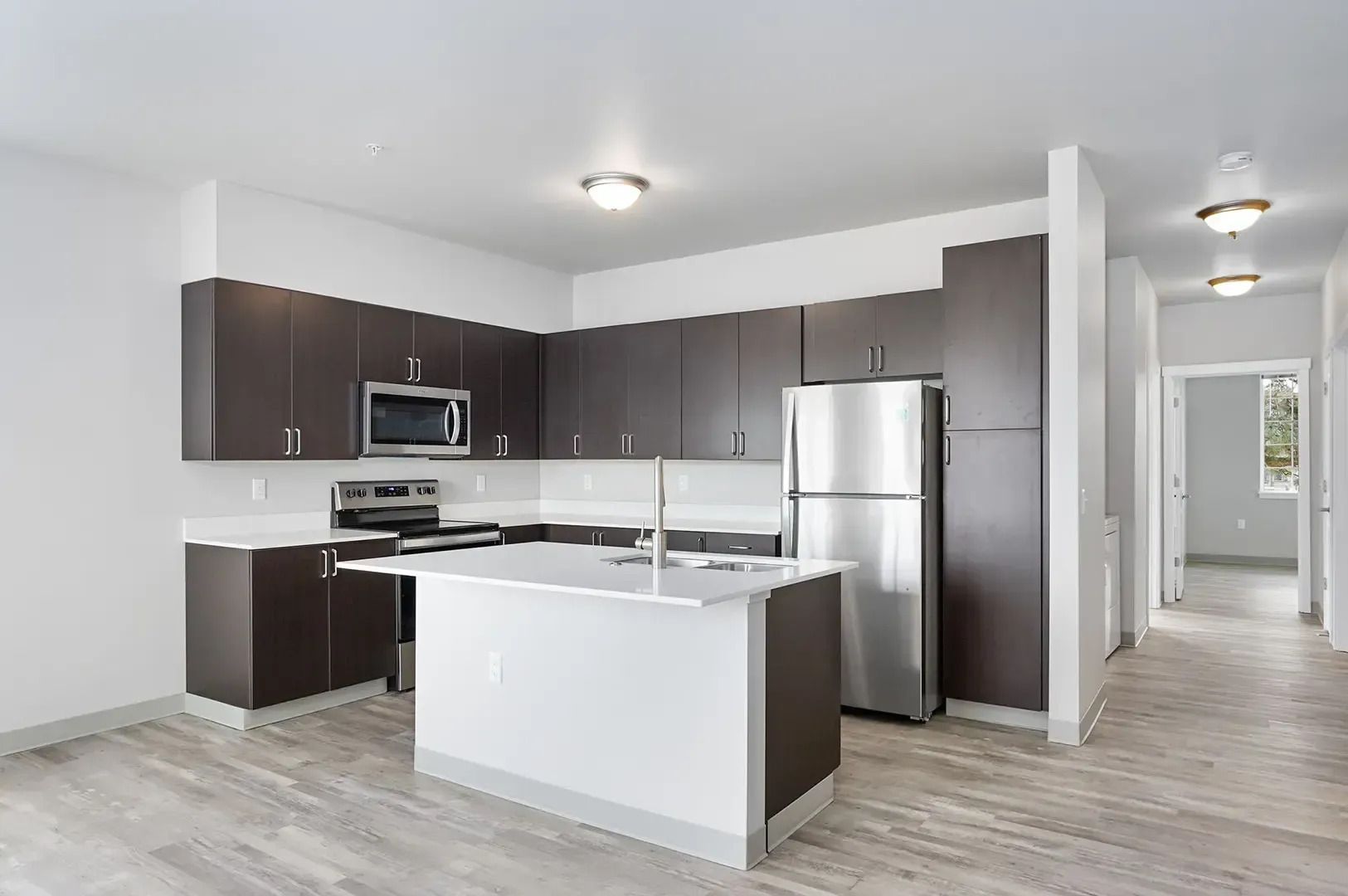 Modern kitchen with dark cabinets, stainless steel appliances, white island, and light wood flooring