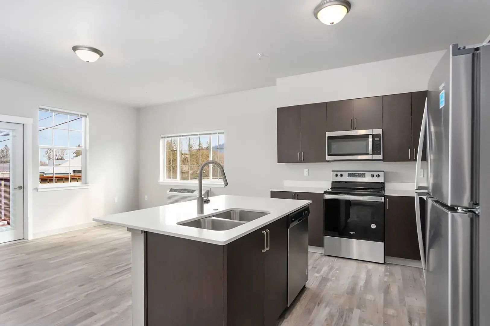 Modern kitchen with stainless steel appliances, dark cabinets, an island, and light wood floors