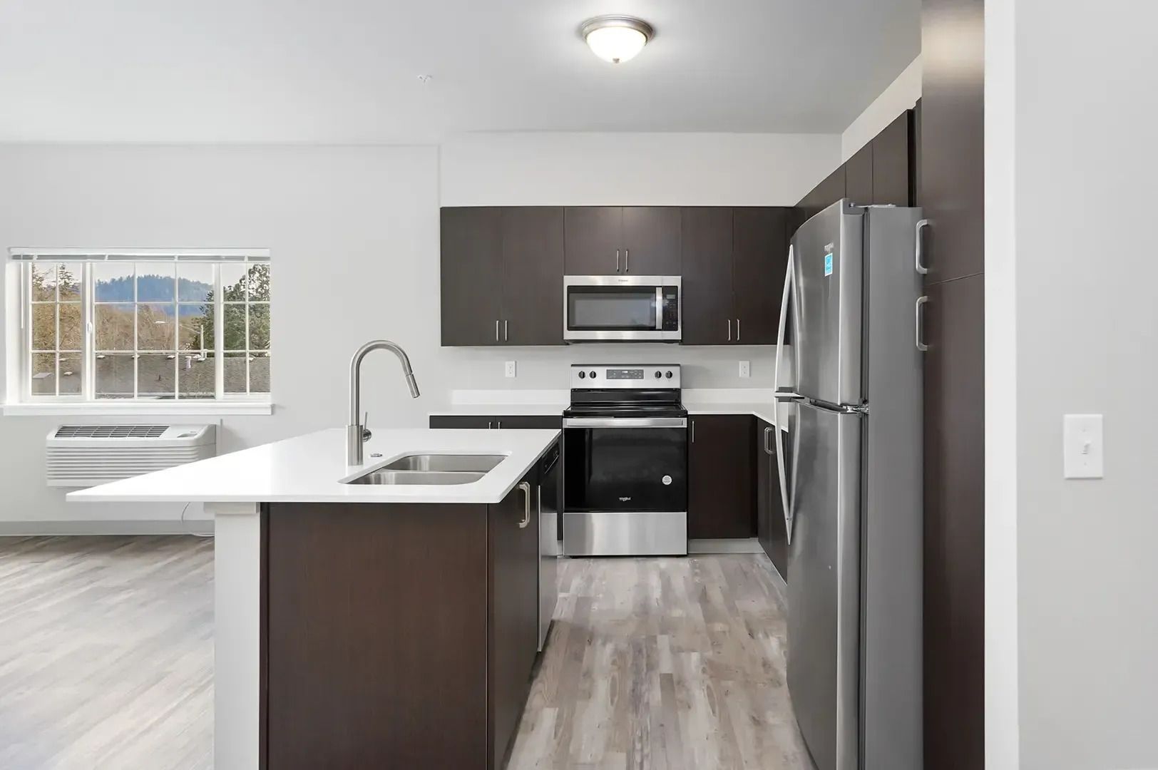 Modern kitchen with stainless appliances, dark cabinets, white island, and large window