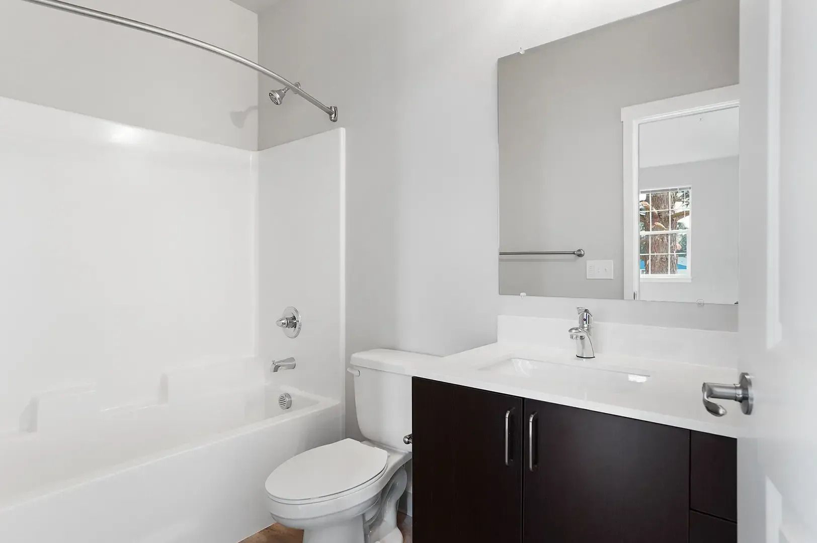 Bright white bathroom with tub, toilet, dark vanity, and large mirror.