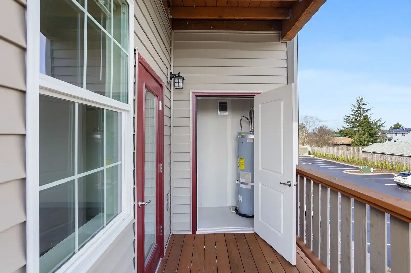 Covered porch with open door revealing a water heater inside, wood railing, and bright outdoor view