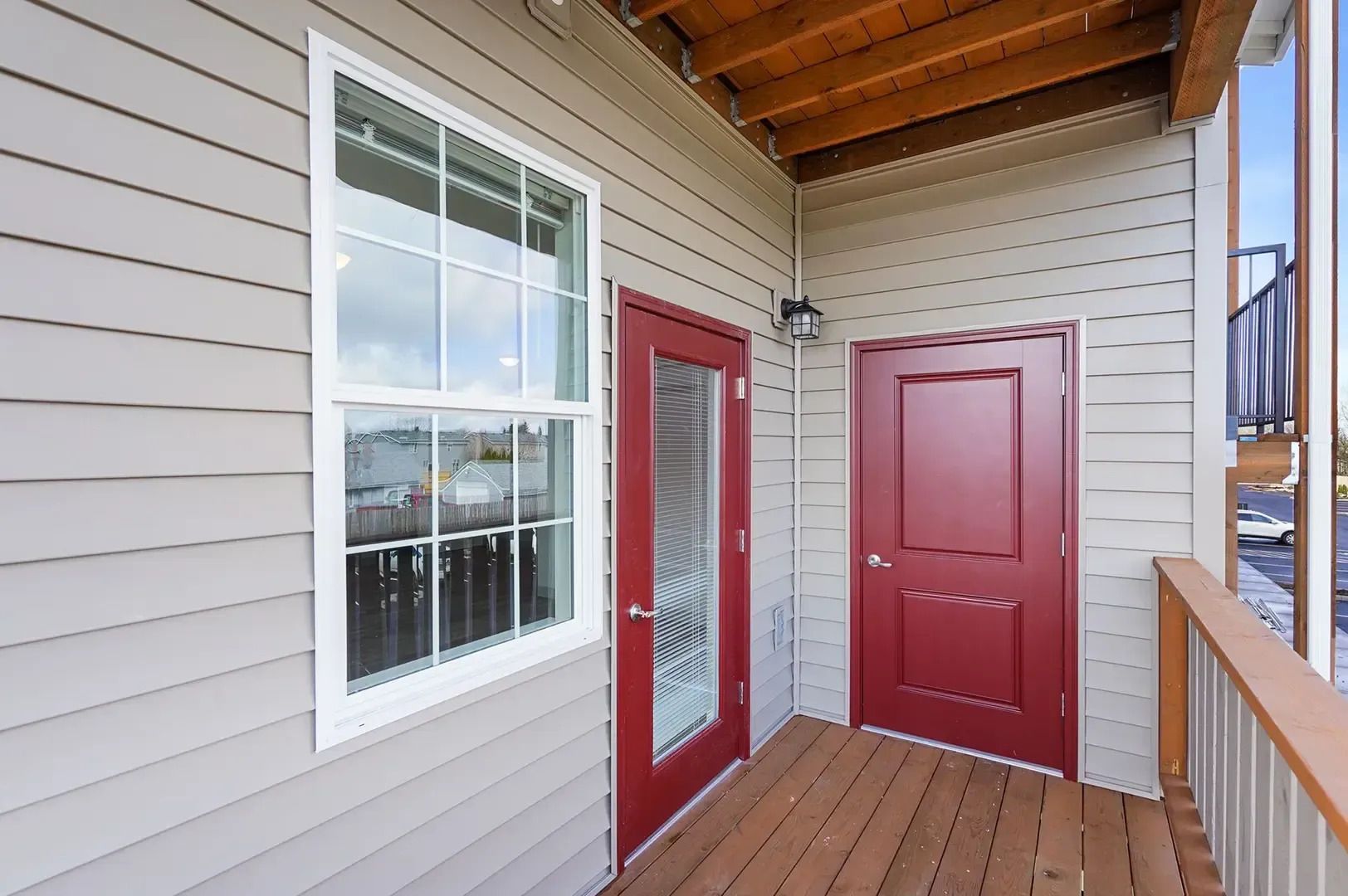 Covered porch with beige siding, red doors, and a large window, viewed from the deck.