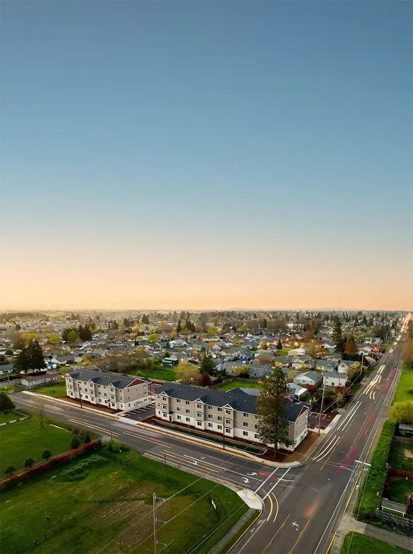 Aerial view of a suburban neighborhood at sunset with rows of houses, streets, and green spaces.