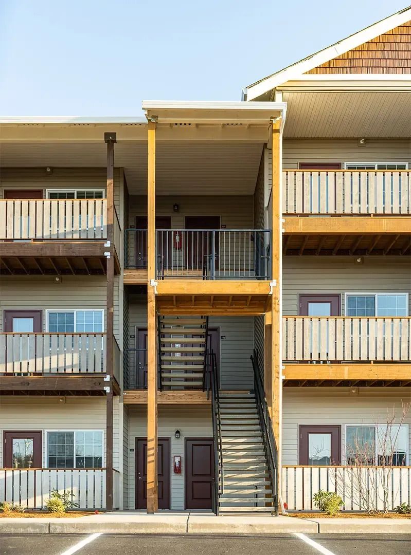 Three-story apartment building facade with balconies and central stairwell under a clear sky