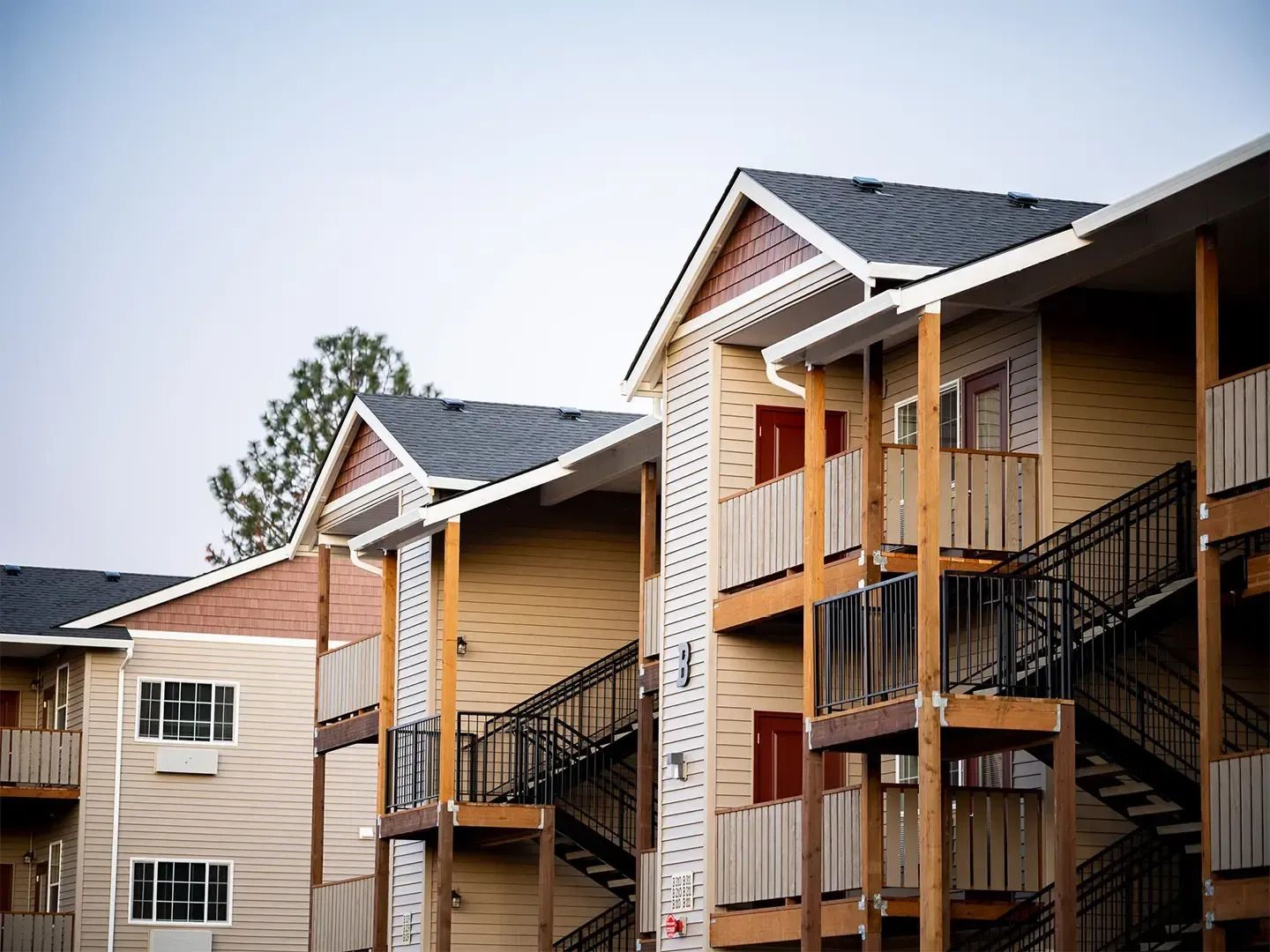 Apartment buildings with beige siding, balconies, and exterior staircases under a blue sky