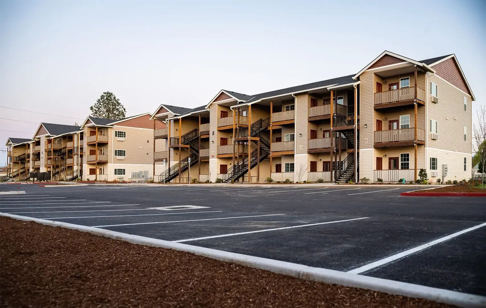 Apartment complex with balconies beside a mostly empty parking lot at dusk