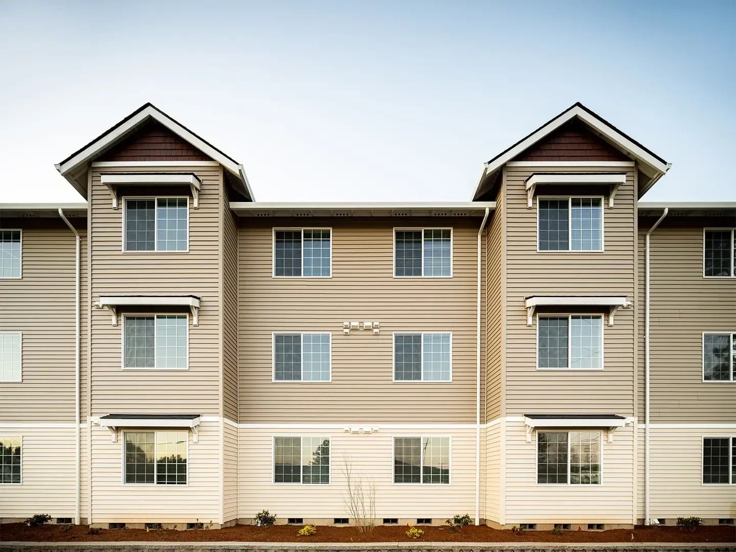 Beige apartment building facade with two peaked roof towers and rows of windows