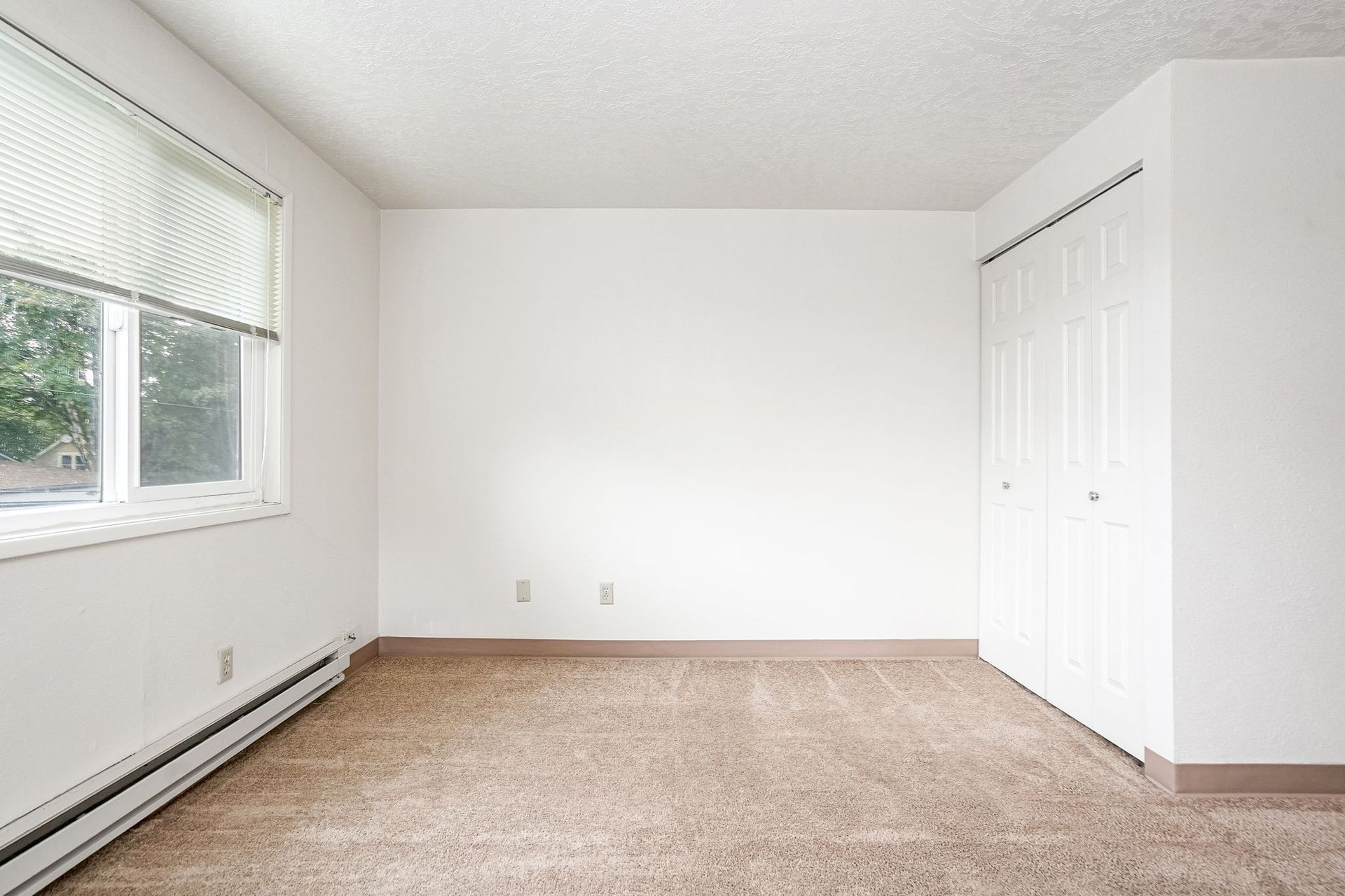 Empty beige bedroom with a window, carpet, and closet doors