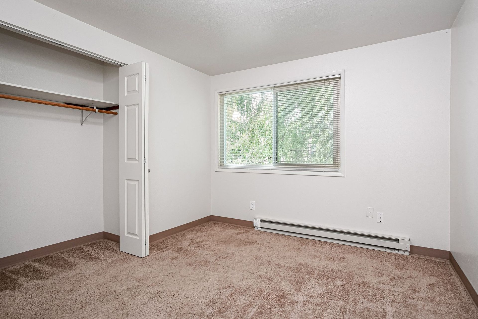 Empty beige bedroom with open closet, window, and baseboard heater