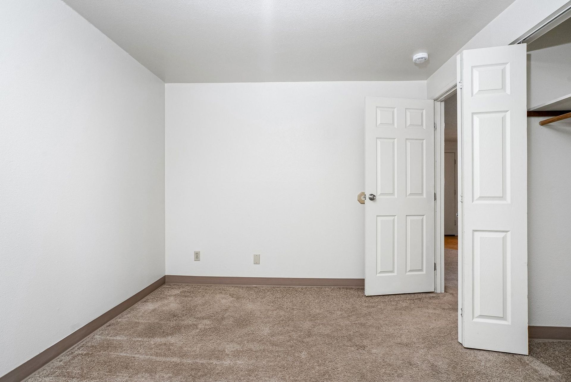 Empty carpeted bedroom with white walls and two open white doors.
