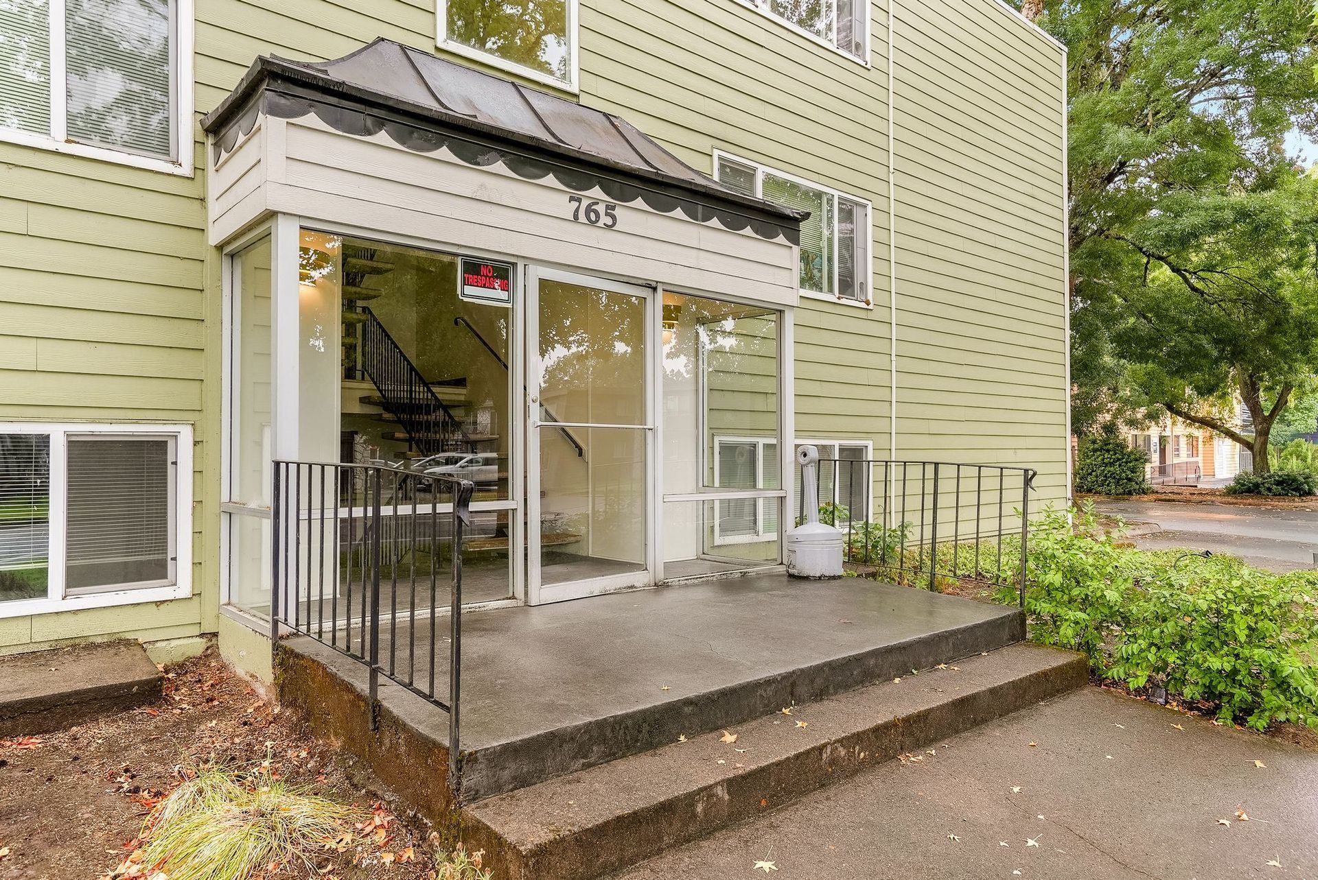 Apartment building entrance with steps, metal ramp, and glass doors under a small awning