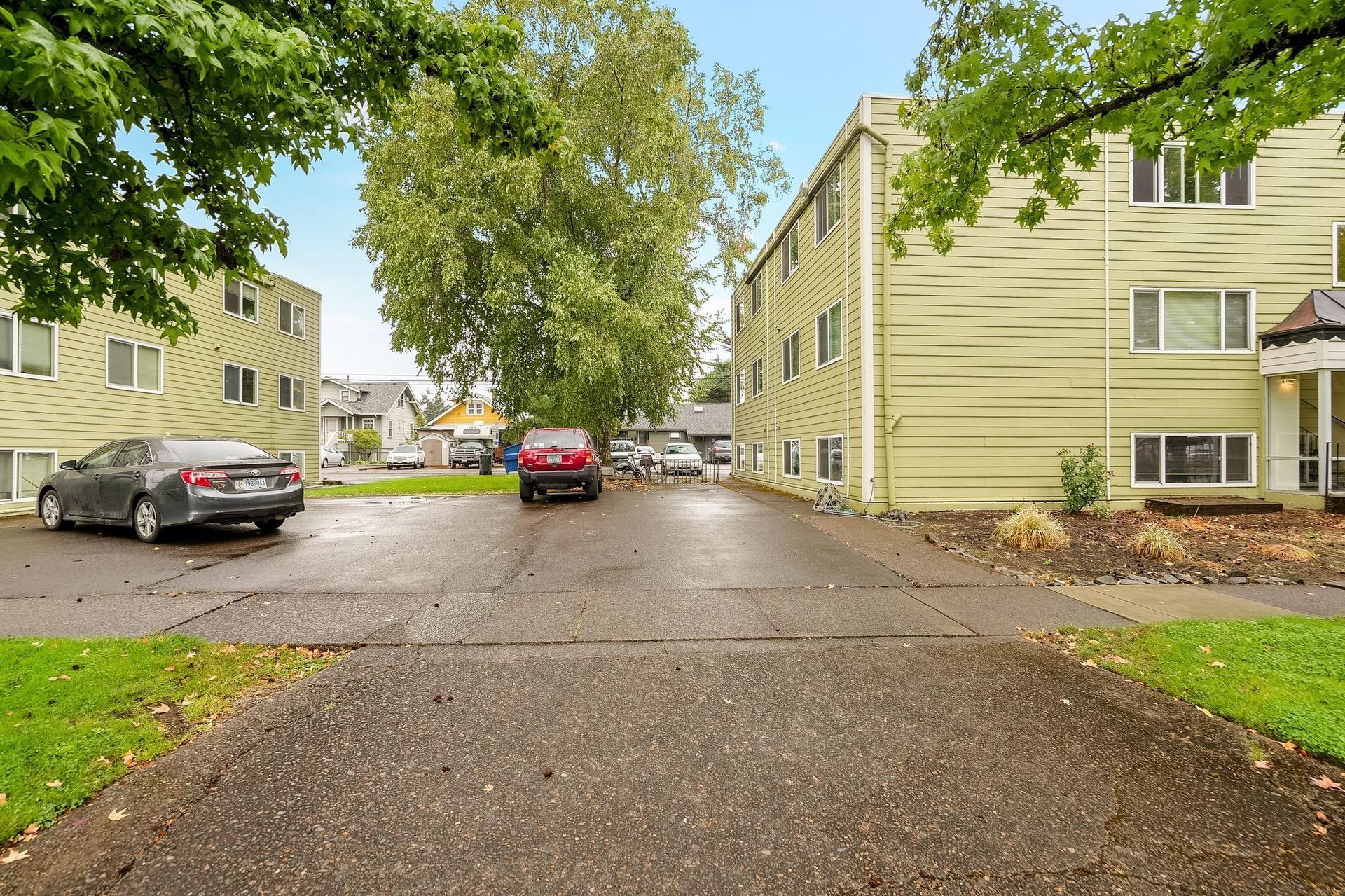 Rainy apartment parking lot with parked cars, trees, and beige buildings
