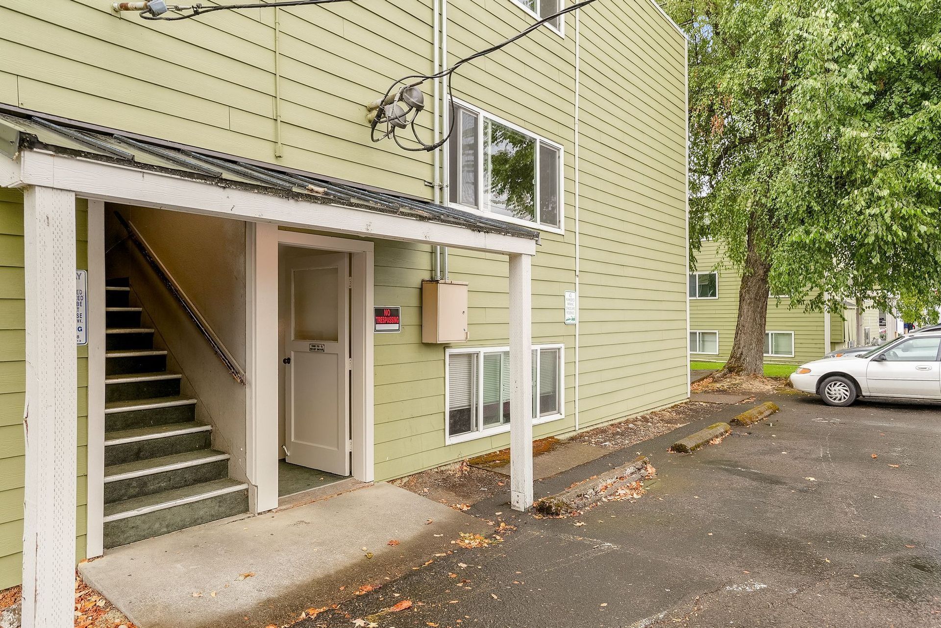 Apartment exterior with covered stairway, beige siding, and parked cars in a lot