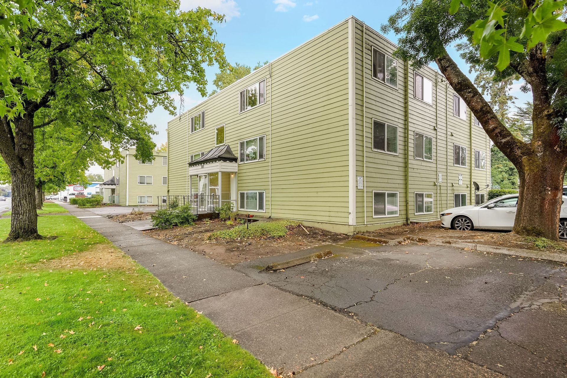 Three-story beige apartment building beside a tree-lined driveway on a cloudy day