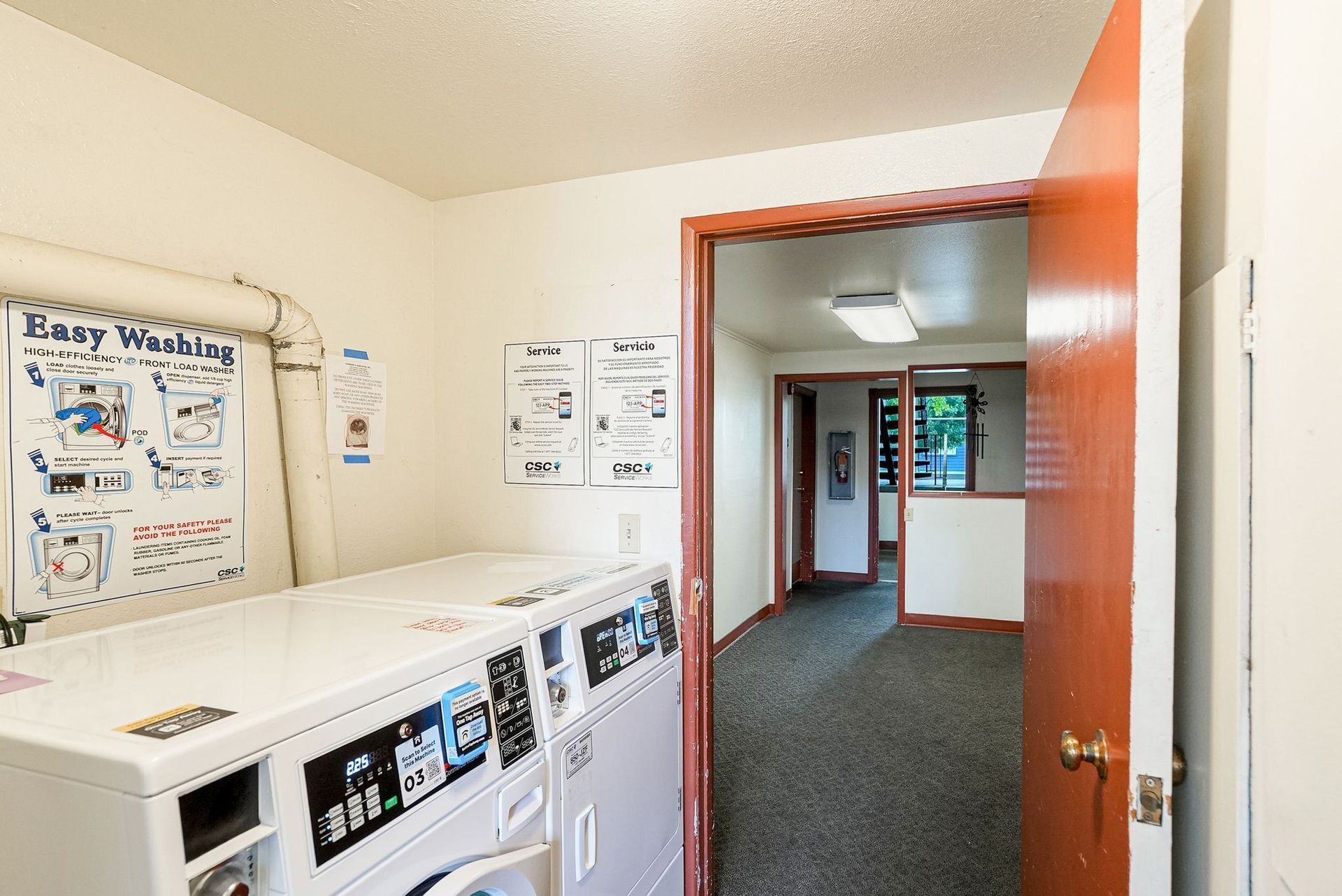 Laundry room with white washers, posters on the walls, and an open doorway to a hallway